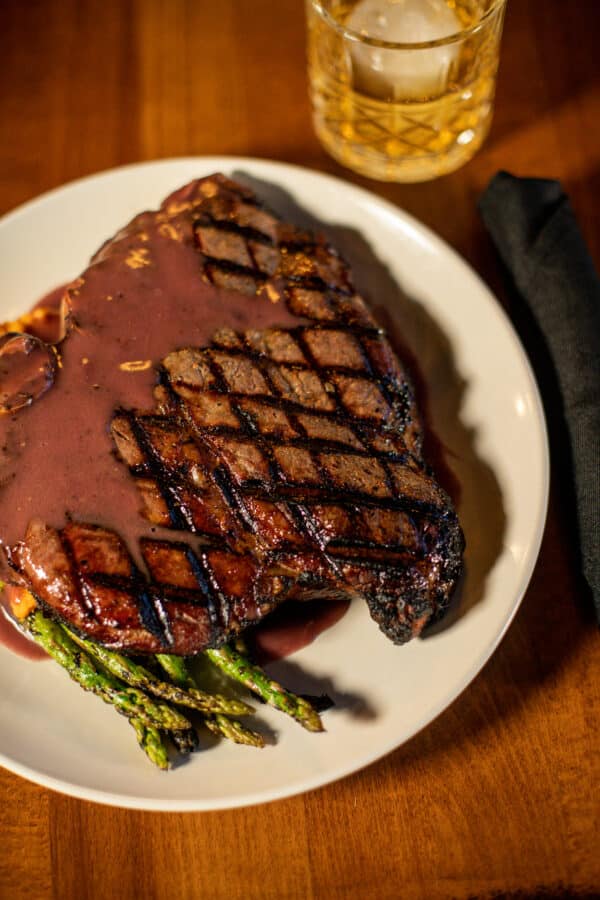 porterhouse steak on a plate with asparagus drizzled with a red colored gravy